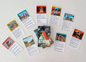 A flat lay of the activity cards for children.  The image shows multiple cards spread out, each with unique artwork and titles like "Conquer With Kindness," "Listen & Create," and "Peace."